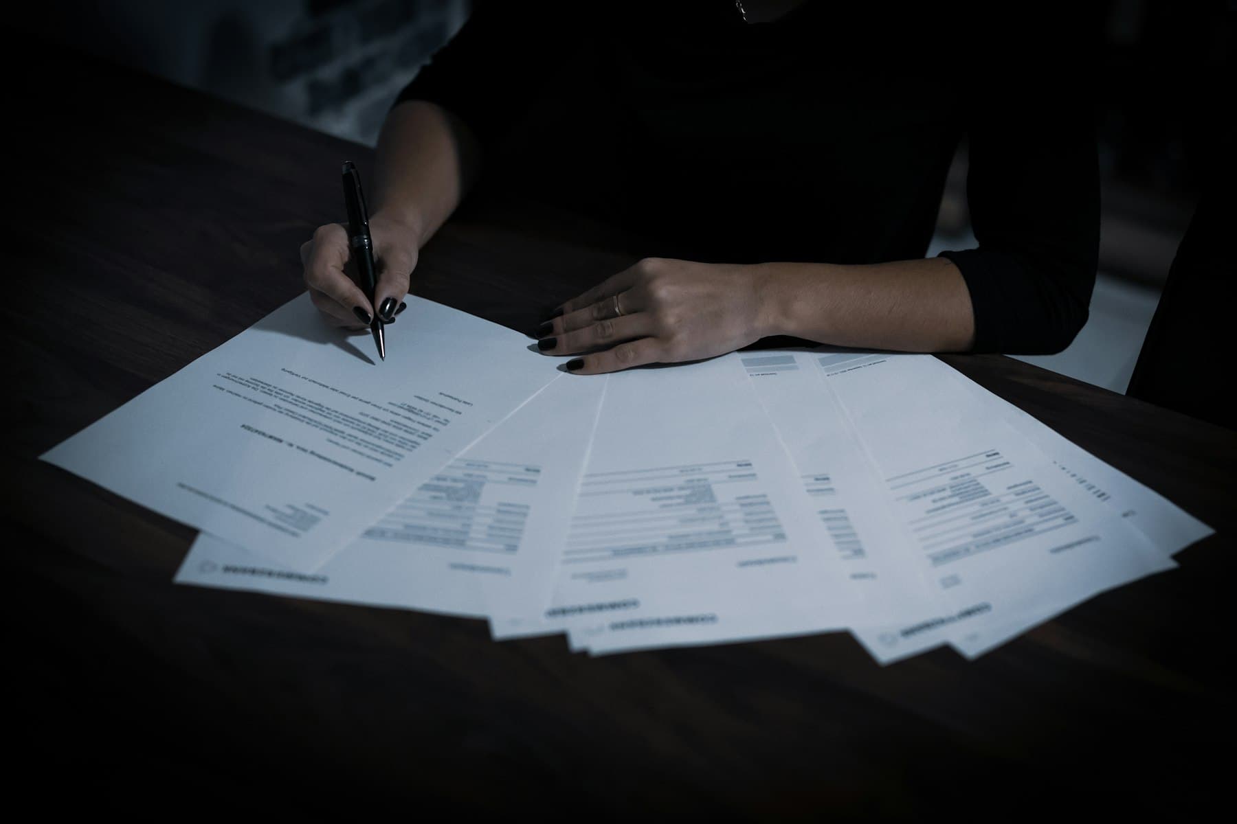 Persona revisando y anotando varios formularios financieros extendidos sobre una mesa.